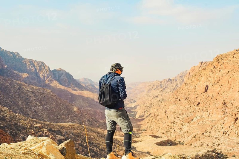 Man trekker standing on cliff edge using mobile phone network coverage vast sandstone valley mountain landscape backdrop hiking travel tech concept Dana Reserve Jordan