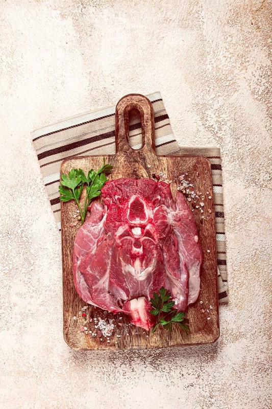 Raw steak, veal neck on the bone, fresh meat, on a cutting board, with spices, top view, without people