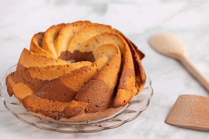 Fresh marble bundt cake, cake next to a rustic wooden spoon on a light-coloured background
