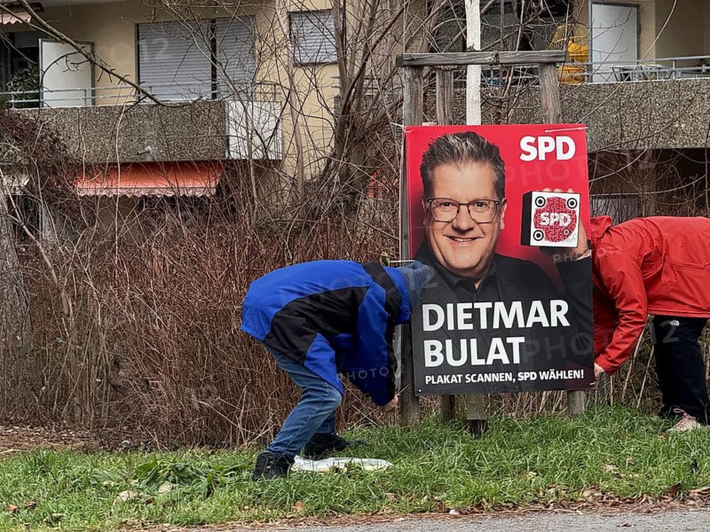 Two people, election workers, fix an SPD election poster on a green area in front of a residential building, election advertising for the 2025 Bundestag election, Sven Bullat, Stuttgart