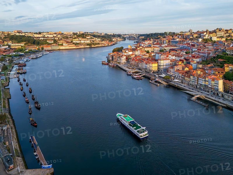 Drone view of Douro River in Porto, Portugal, with a tourist boat between Ribeira and Vila Nova de Gaia, with moored rabelo boats at sunrise