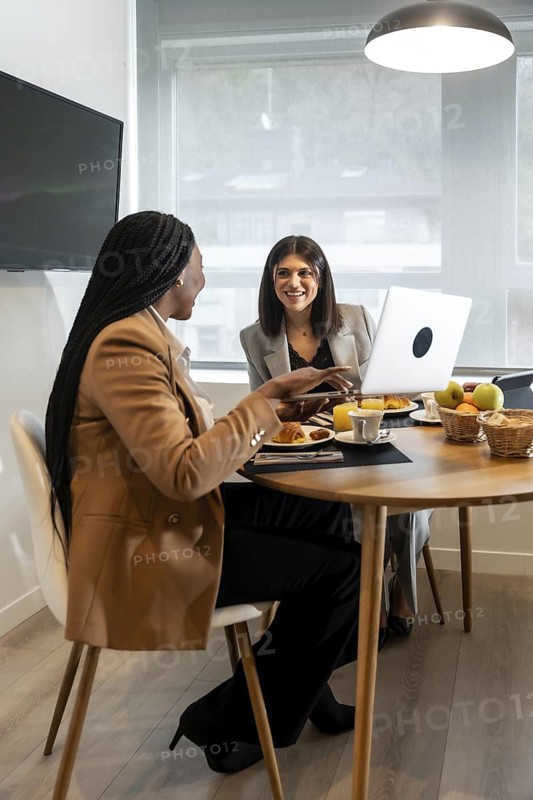 Two businesswomen enjoying breakfast and working on a laptop during their stay at a hotel