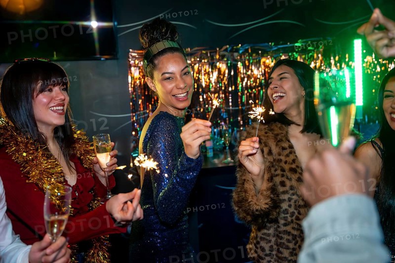 Diverse friends enjoying a festive party atmosphere, holding sparklers and glasses of champagne, laughing and celebrating together in a vibrant nightlife setting