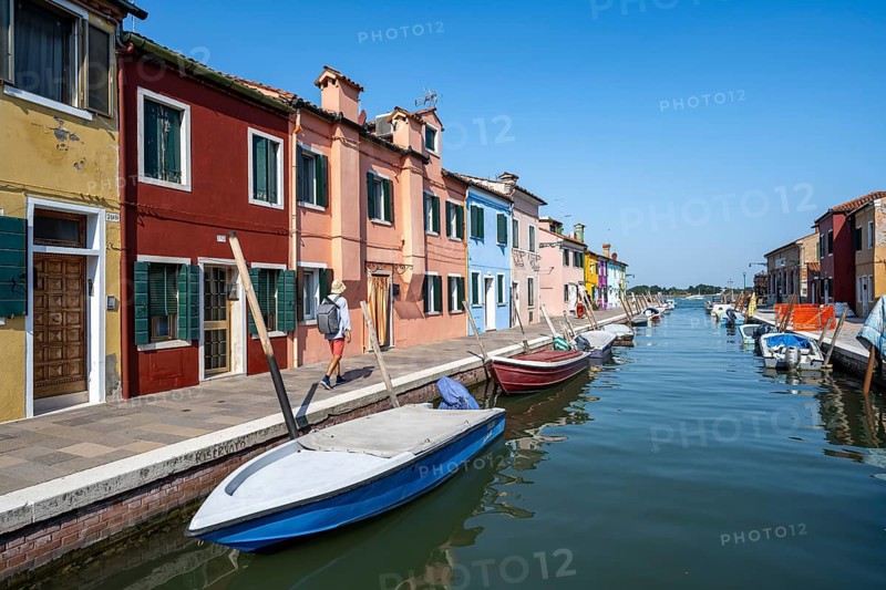 Young man in front of colourful houses on the canal, canal with boats and colourful house facades, Burano Island, Venice, Veneto, Italy