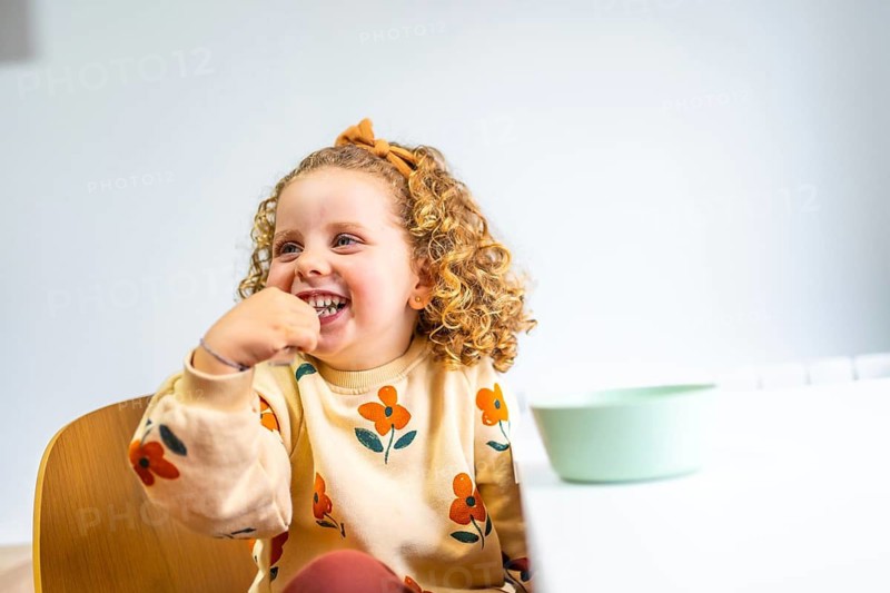 Cute blonde caucasian little girl eating without help smiling at home