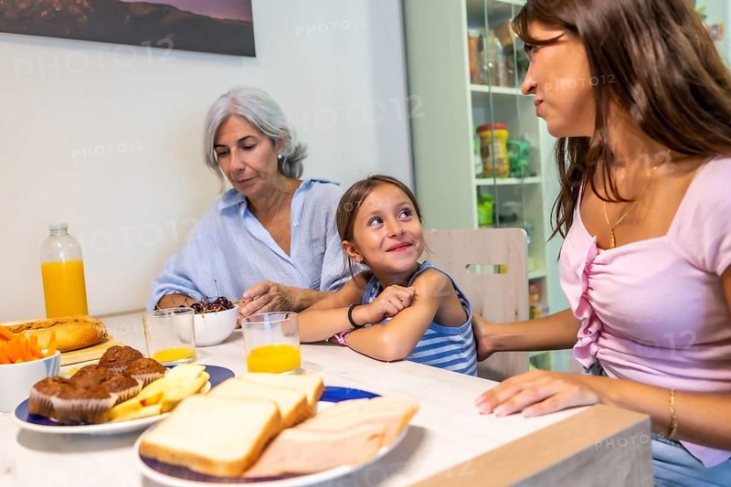 Multi generational women sitting around a kitchen table, enjoying a casual breakfast with food and drinks, sharing a moment of family bonding and daily life at home