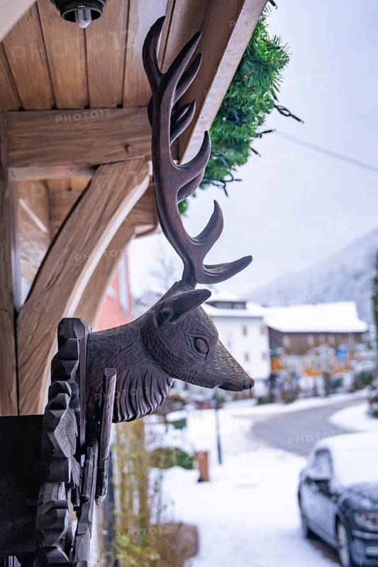 Wooden sculpture of a stag's head on a house in the snow, Enzklösterle, Calw district, Black Forest, Germany
