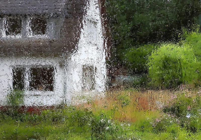 Raindrops on a window pane with indistinct view of a house with trees in summer, Witten, North Rhine-Westphalia, Germany
