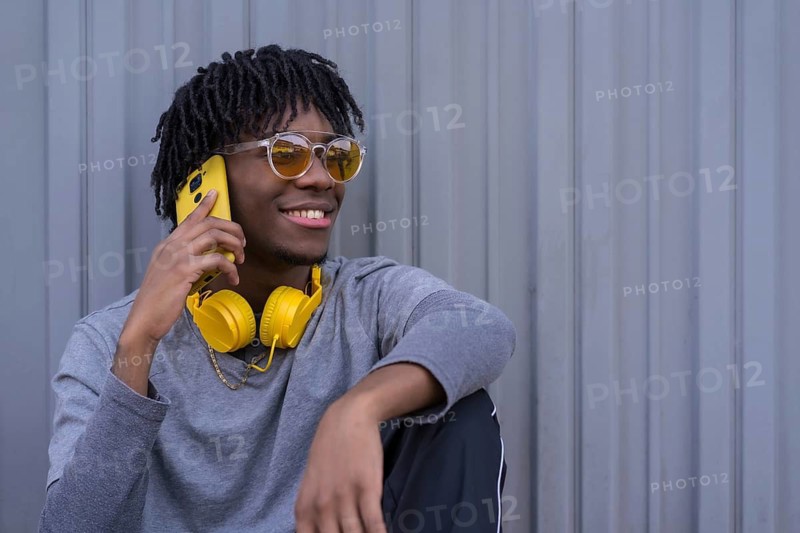 Portrait with copy space of a young african man taking to the mobile sitting on the street