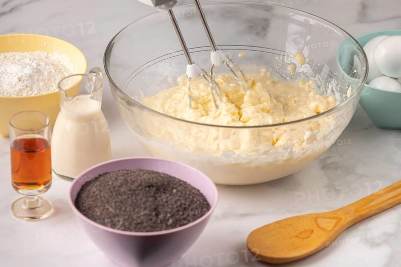 Baking ingredients are mixed in a bowl, surrounded by other ingredients such as poppy seeds and rum