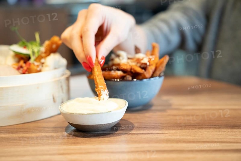 Hand dipping sweet potato fry into sauce on wooden table