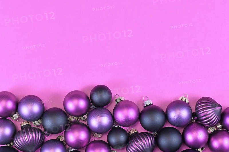 Seasonal dark purple and pink Christmas tree bauble ornaments at bottom of pink background with empty copy space