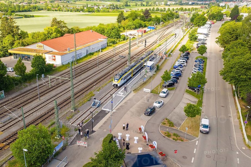A train station with a stopping train, parked cars and people on a sunny street, inauguration of the Hermann Hesse Railway extension, Renningen, Böblingen district, Germany