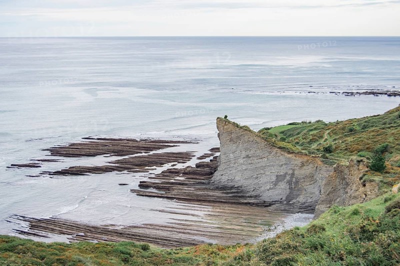 Scenic view capturing the rugged beauty of coastal cliffs as they meet the calm ocean, showcasing layers of geological formations amidst lush greenery