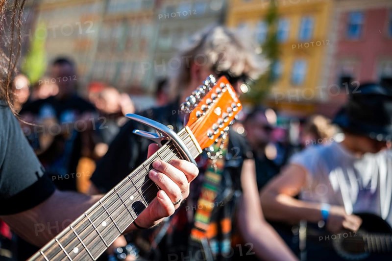 Close-up shot of a musician playing a 12-string acoustic guitar with a capo during an outdoor street performance, focusing on the left hand and the headstock in Wroclaw, Poland