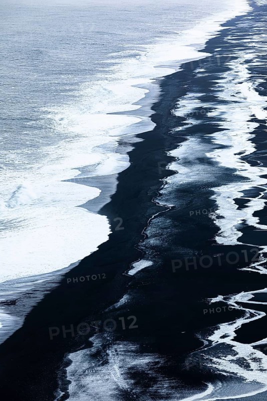 Foamy white waves and icy surfaces on the black pebble beach Skogarsandur, near Dyrholaey, Sudurland, Iceland