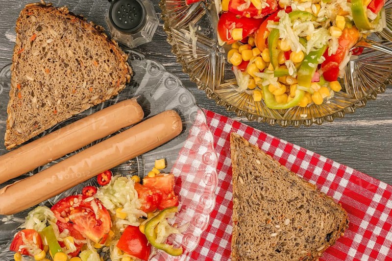 Sausages with bread and vegetable salad on a picnic table