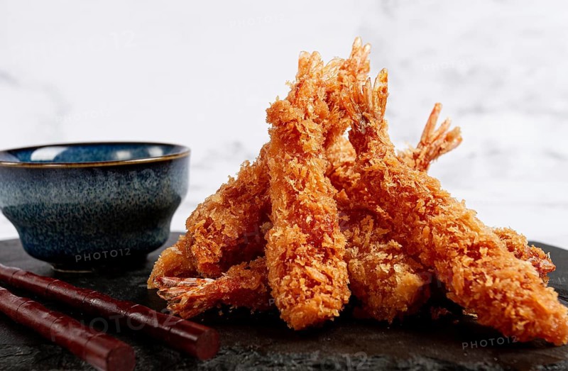 Shrimp in tempura, deep fried, on black slate, with sauce, light marble table, no people