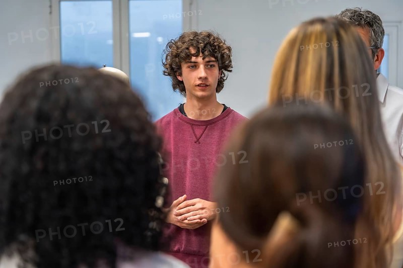 Young male student is actively participating and speaking to his classmates and teacher during a group discussion in a modern educational classroom setting