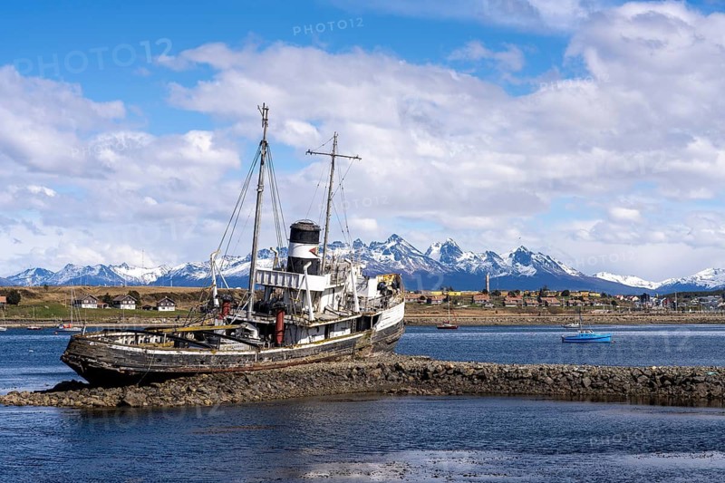 Shipwreck of the Saint Christopher steam tug stranded on rocks in the harbor, behind small sailboats and snow-capped mountains of the Martial Range, Ushuaia, Tierra del Fuego, Argentina