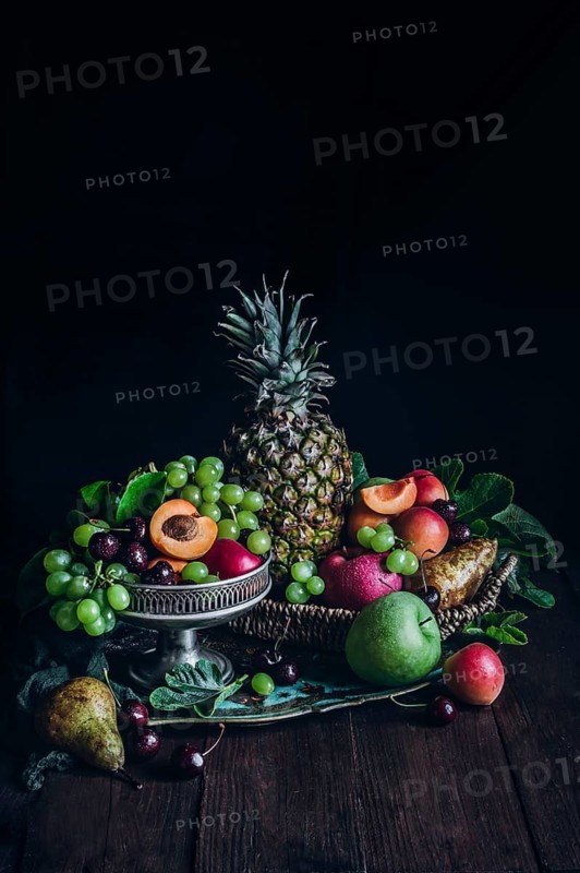 A lush arrangement of fresh tropical fruits including pineapple, apricots, grapes, and cherries, artfully presented in baskets and on wooden surfaces, highlighting nature's bounty