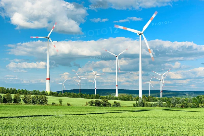 Green wheat field and wind turbines under a blue sky with cumulus clouds, in the background the Fahner Höhe, near Bad Langensalza, Thuringia, Germany
