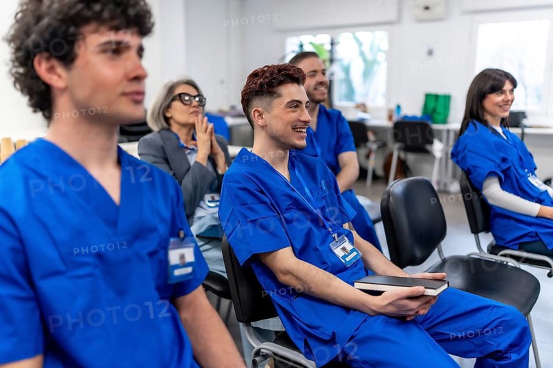 Young medical students and an experienced trainer sitting in a classroom, listening attentively with smiling faces during a vocational training session on healthcare education