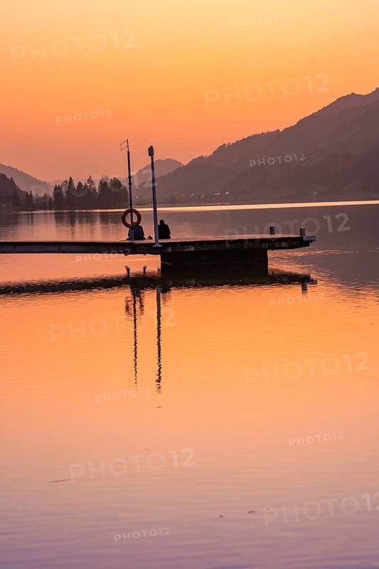 Footbridge at dusk, silhouettes of people on a quiet lake surrounded by mountains, Großer Alpsee, Immenstadt im Allgäu, Bavaria, Germany
