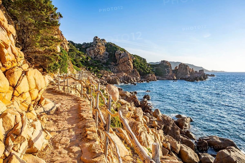 A little trail passing the rocks at the coastline with blue water at Costa Paradiso on a sunny day at sunset, Sardinia, Italy