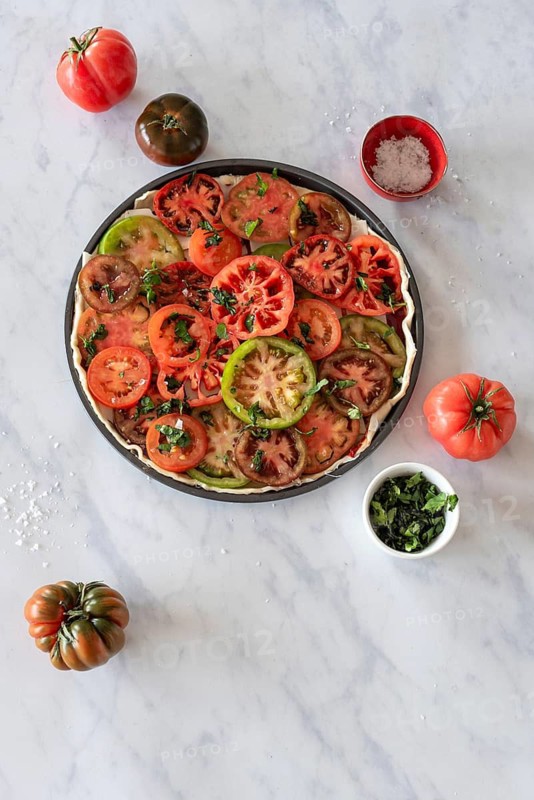 A vibrant salad featuring sliced heirloom tomatoes garnished with fresh herbs. Presented on a marble surface, this dish is ideal for a refreshing and healthy meal