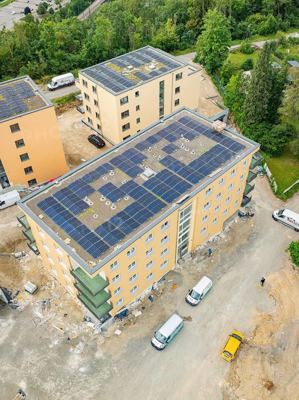 Aerial view shows buildings with solar panels on the roofs, construction site with several vehicles and surrounded by numerous trees, Horb, Black Forest, Germany