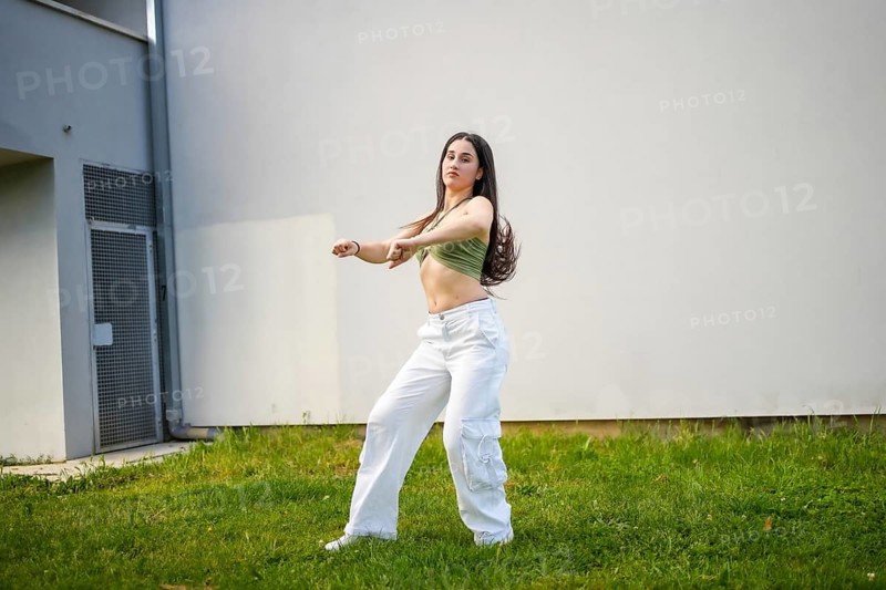 Beauty caucasian young female dancer performing modern choreography outside a building with grass
