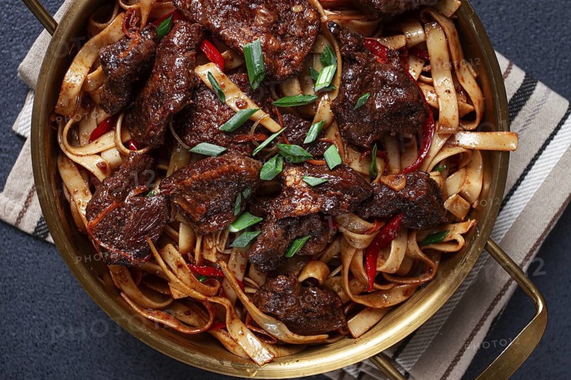 Udon noodles with Mongolian beef, green onions and vegetables, in a brass pan, on a gray background, homemade, no people