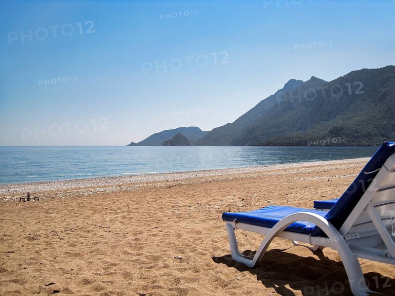 Picturesque beach of Çirali on Turkey's Mediterranean coast with an empty blue sun lounger and steep coastal mountains on the horizon, views of the Mediterranean Sea, coastline, Cirali, Olympos, Kumluca, Lycian Way, Lycia, Antalya, Turkey