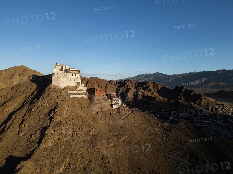Captivating view of Leh Palace in Leh Ladakh, India, perched atop a rugged hill with a backdrop of breathtaking mountains under a clear blue sky, showcasing architectural grandeur