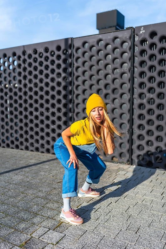 Young woman showcasing her urban dance moves in a dynamic pose, wearing a yellow beanie, t shirt, and denim overalls