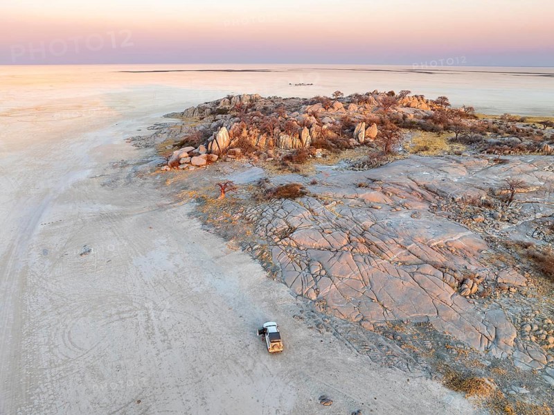 Rocky island with baobab trees in a dry salt pan, at sunset, off-road vehicle on the salt pan, aerial view, Kubu Island, Botswana