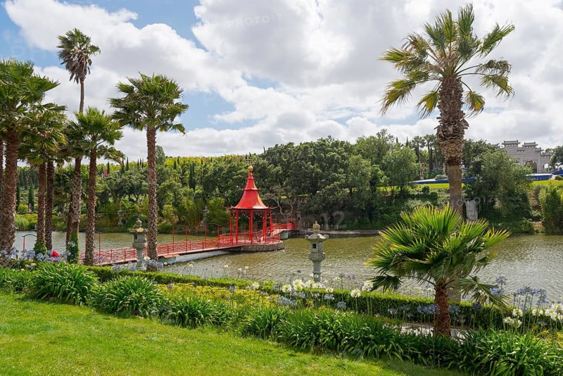A red pavilion and palm trees by a pond, surrounded by lush, green nature under a cloudy sky, Bacalhôa, Bacalhoa Buddha Eden, Quinta dos Loridos, largest oriental garden in Europe, Bombarral, Oeste, Centro, Portugal