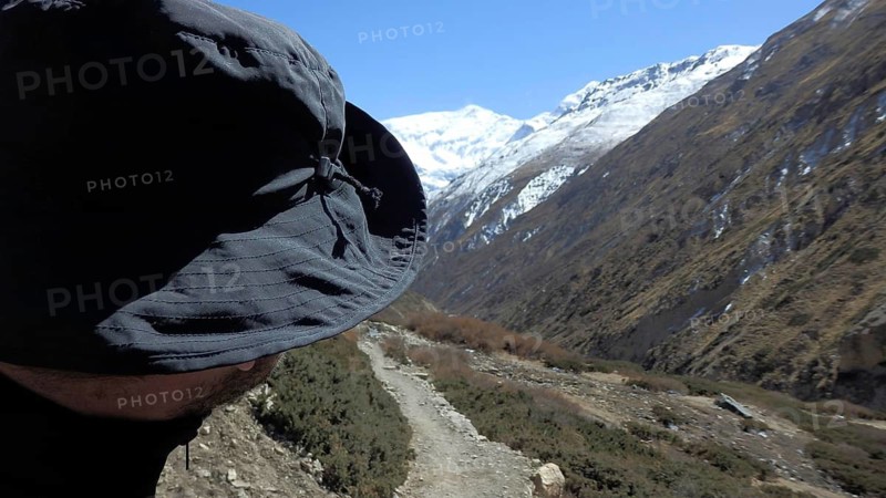 Person wearing hat looking at a majestic mountain landscape with snow-capped peaks, trekking at Annapurna Circuit, Manang, Nepal