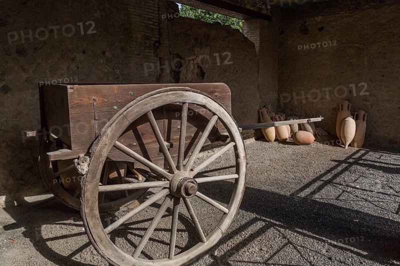 Old wooden cart and ceramic jugs on display inside an unenclosed building at the ancient ruins of Pompeii, Campania region, Italy