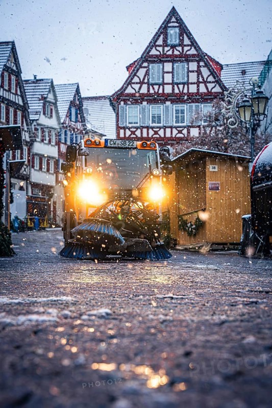 Clearing vehicle at work at a Christmas market during a snowfall in the evening, Black Forest, Calw, Germany