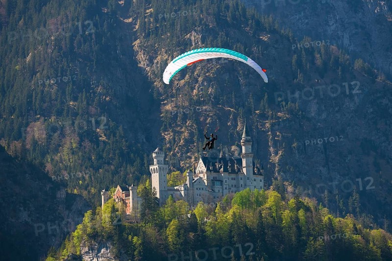 A paraglider flies over Neuschwanstein Castle against a mountain backdrop, Schwangau near Füssen, Ostallgäu district, Swabia, Bavaria, Germany