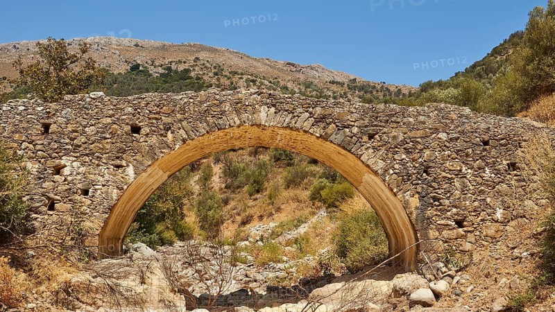 Old stone bridge in front of a mountain panorama with dry terrain under clear sky, Amari Basin, Amari, Central Crete, Greek Islands, Greece
