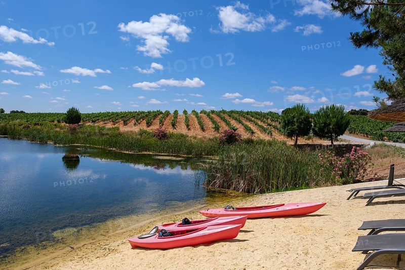 Two red kayaks lie on the sandy shore of a clear lake under a blue sky, Pedrógão, Beja, Portugal