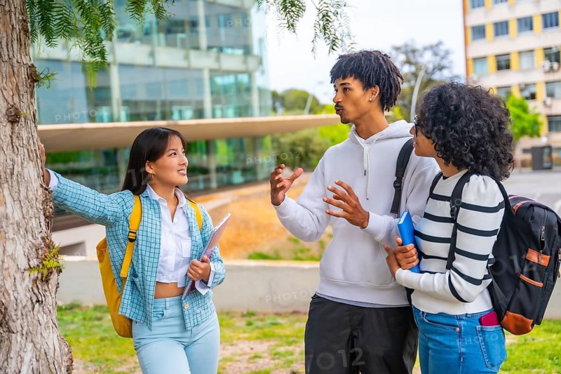 Three multi-ethnic friends talking leaning on a tree in the university