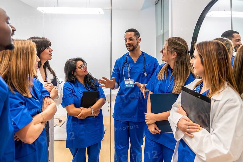 Healthcare professionals in scrubs and lab coats actively listening to a male doctor, sharing insights and working together in a hospital or clinic setting