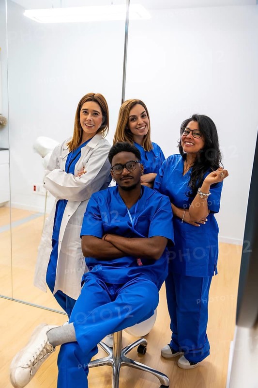 Diverse group of medical professionals smiling, standing and sitting confidently in a clean white clinic environment, representing collaboration and dedicated patient care