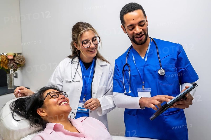 Healthcare professionals consulting with a happy female patient in a medical office, explaining health information and treatment options using a digital tablet for modern, collaborative care