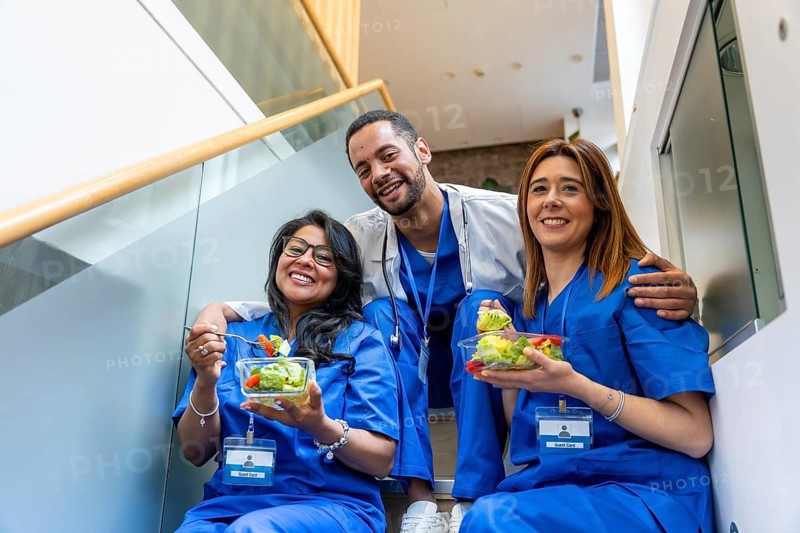 Healthcare professionals relaxing and enjoying a nutritious salad meal together on a staircase during their break, promoting wellness and teamwork in a modern medical facility