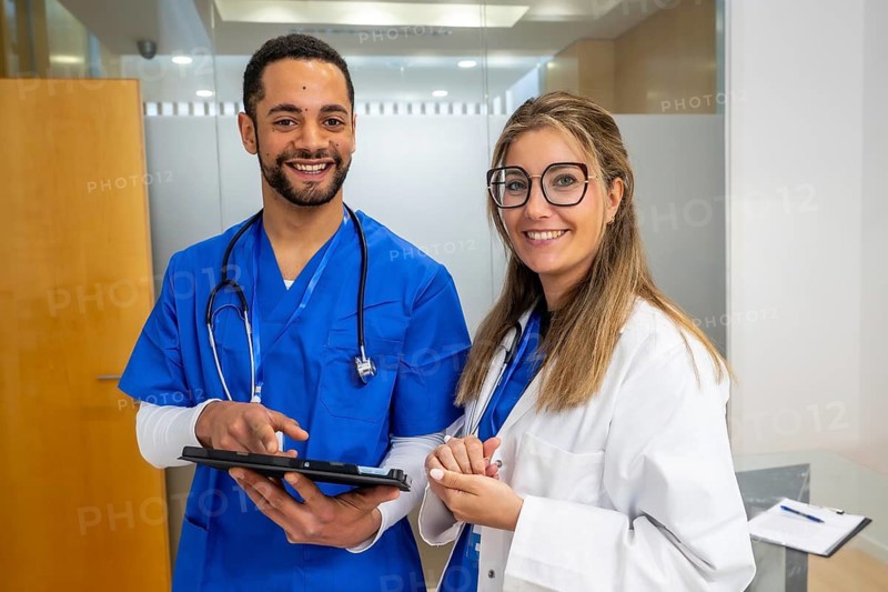 Diverse medical professionals smiling while reviewing patient information on a digital tablet in a modern hospital or clinic, representing teamwork and health technology